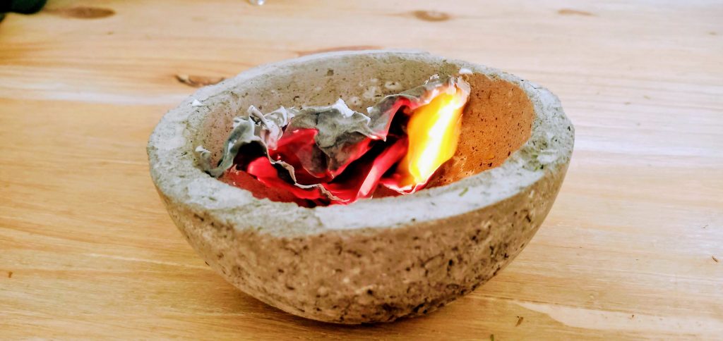 Papel que arde dentro de un cuenco de cemento sobre una mesa de madera